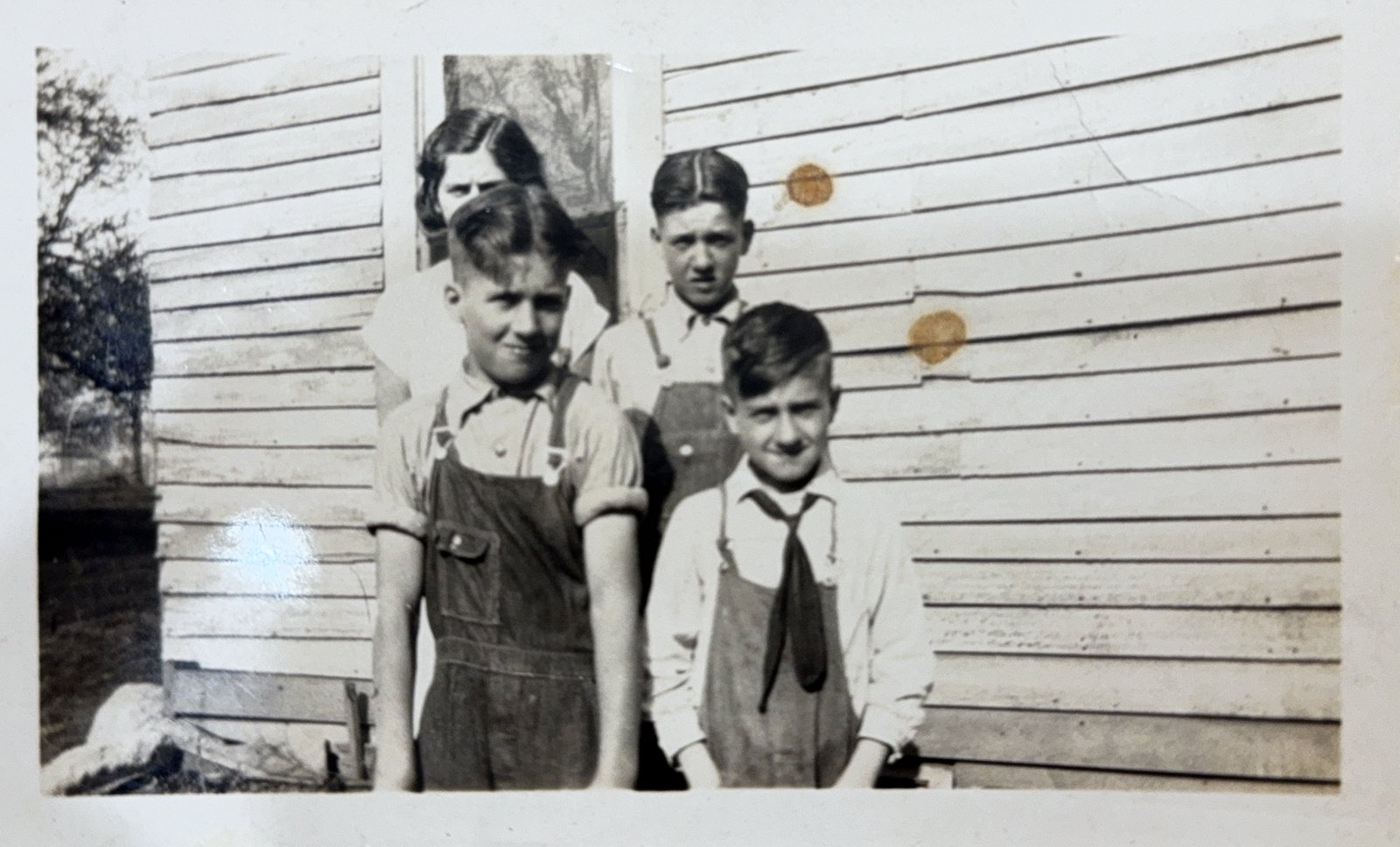 Four boys standing against a clapboard farmhouse